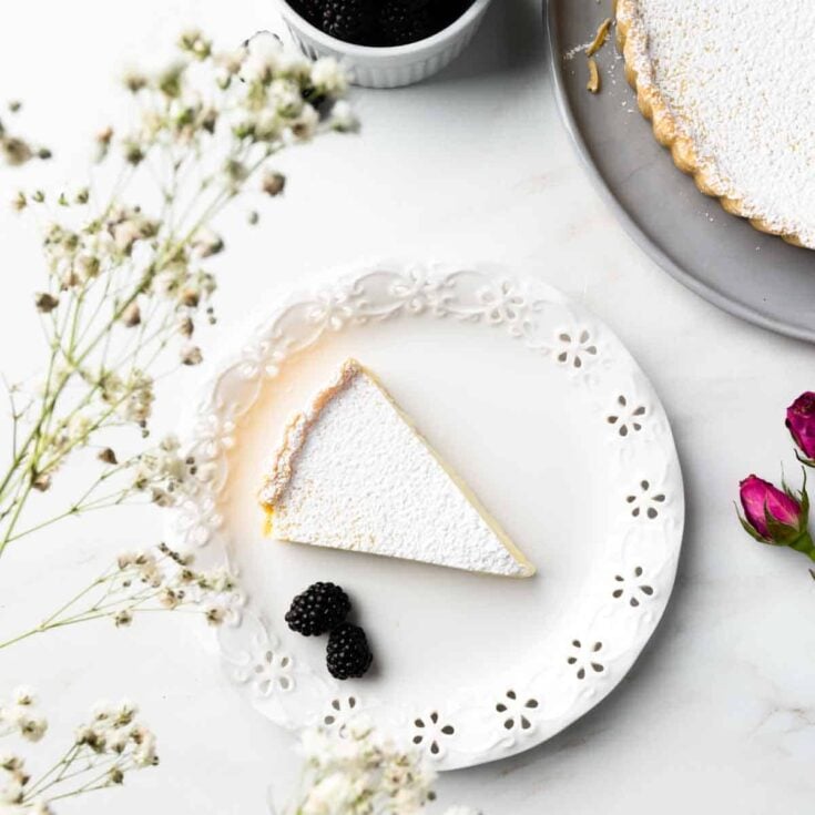 A slice of ricotta pie and two fresh black berries on a round white plate.