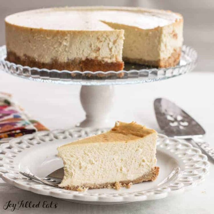 Vanilla ricotta cheesecake on a cake stand with one slice taken out and placed on a white serving plate.