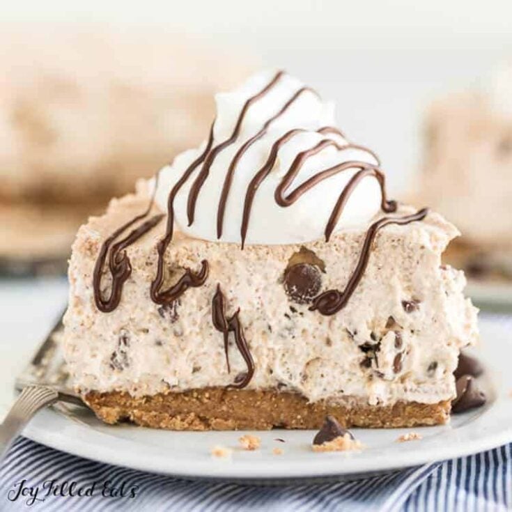 A slice of cannoli cheesecake topped with whipped cream and a chocolate drizzle on a white plate.
