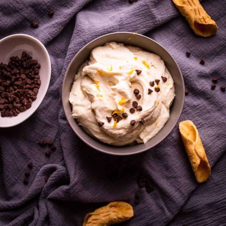 A large bowl with cannoli filling topped with mini chocolate chips and fresh orange zest.