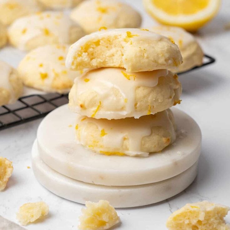 Three lemon ricotta cookies stacked on top of each other and the top one with a bite missing from it.
