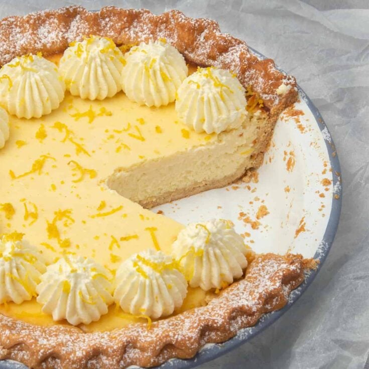 Ricotta pie in a round pie plate topped with lemon zest with one slice missing.