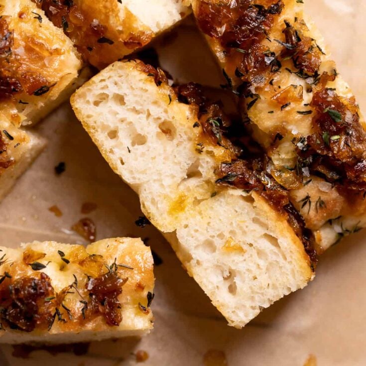 Three slices of caramelized onion focaccia bread on brown parchment paper.