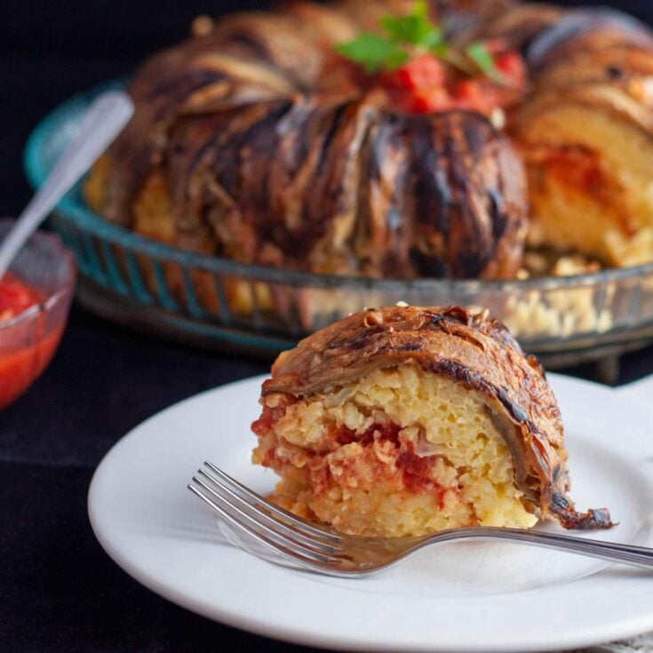 A large eggplant rice timbale with a slice cut out and placed on a white serving plate with a silver fork.