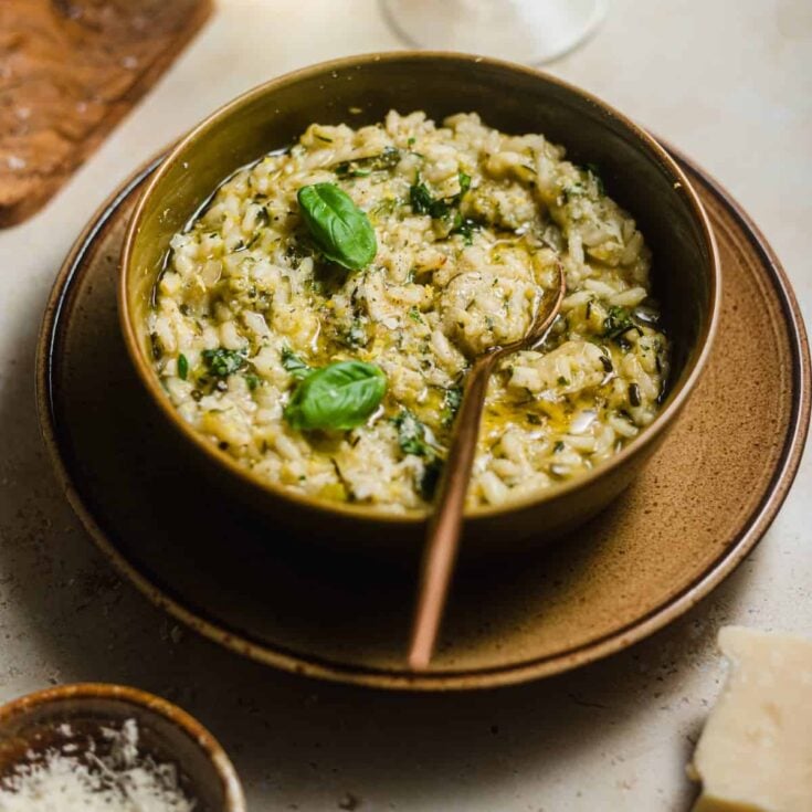 A brown serving bowl with zucchini risotto topped with two fresh basil leaves.