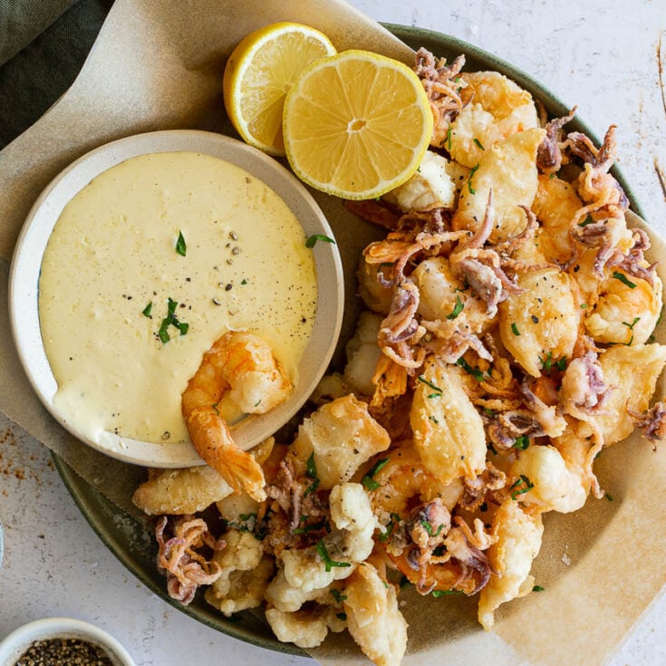 A large bowl of fritto misto with an aioli dipping sauce and two lemon halves.