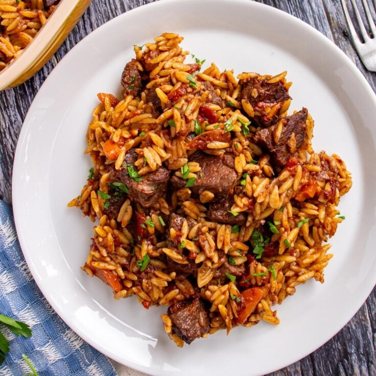 A large white plate with cooked beef, orzo and carrots garnished with fresh parsley.