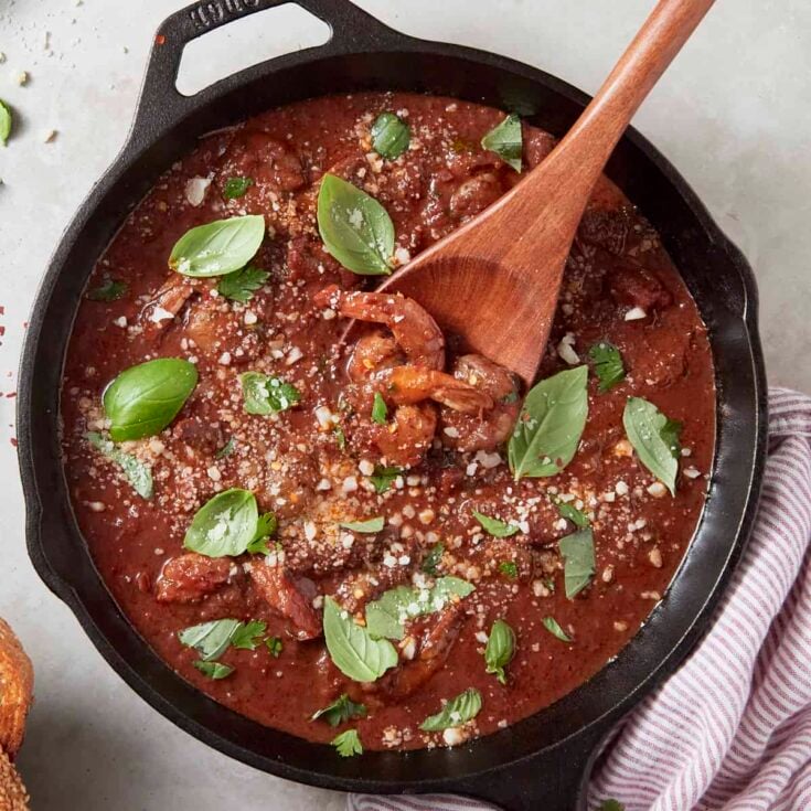 Shrimp fra diavolo in a large cast iron skillet garnished with fresh basil leaves.