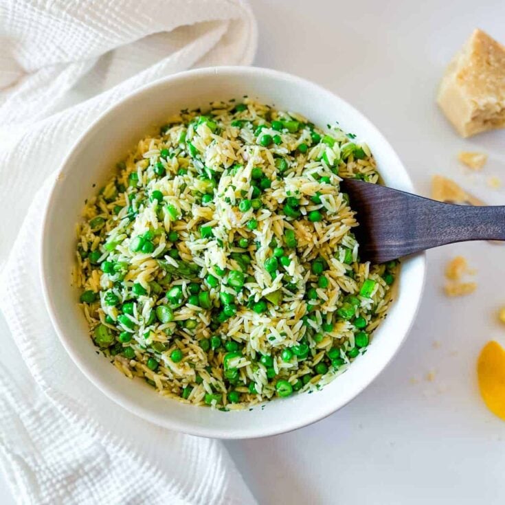 A white bowl with orzo, diced asparagus and green peas.