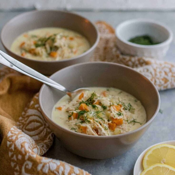 Two gray bowls with cooked chicken, orzo pasta, onions, celery and carrots in a creamy broth topped with fresh dill.