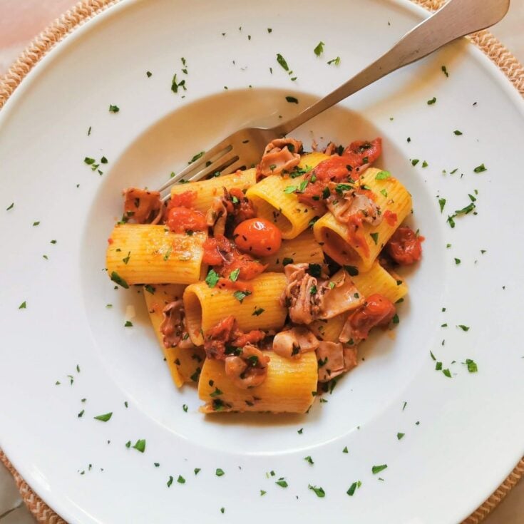 Pasta with calamari and tomatoes in a white serving bowl garnished with parsley.