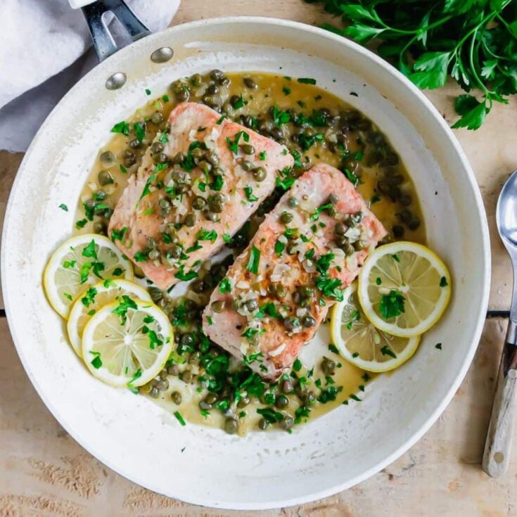 Salmon piccata garnished with capers, parsley and slices of fresh lemon.